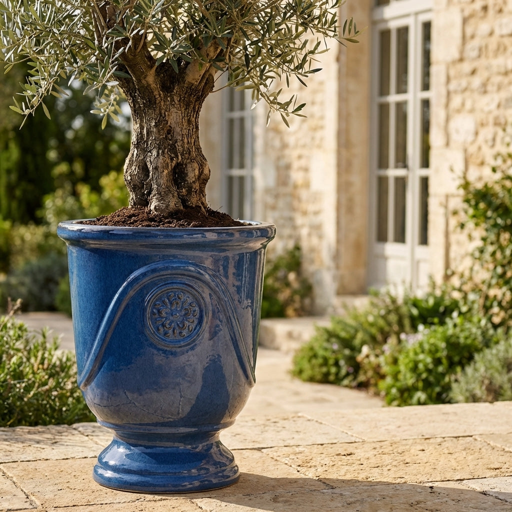 Detail ručně vyráběného glazovaného keramického květináče Moliere Anticky modrý z terakoty s ozdobným reliéfem a olivovníkem na slunné terase.