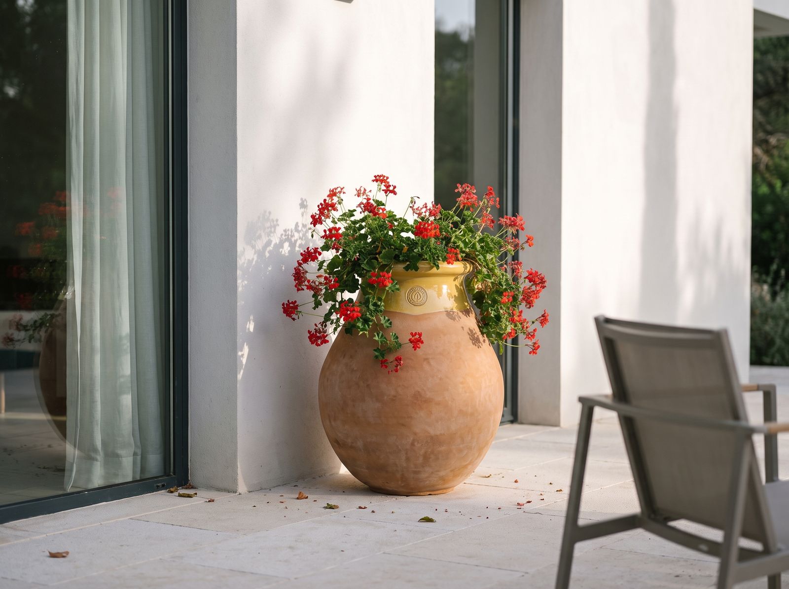 Biot mit roten Pelargonien auf der Terrasse einer modernen Villa
